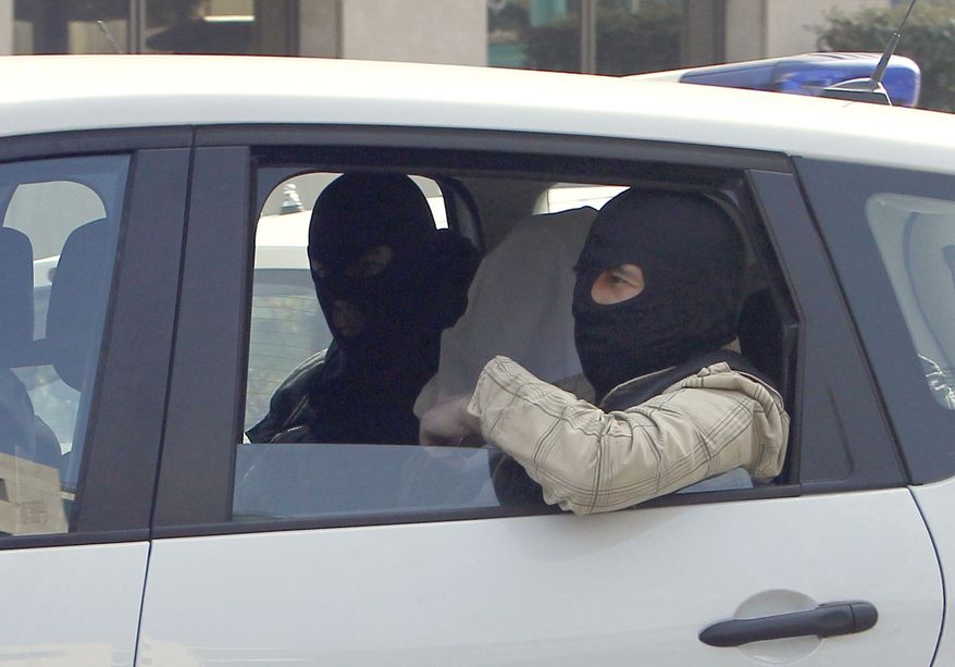 An unidentified man with his head covered, believed to be Abdelkader Merah or his companion, sits between masked police officers as they head to the French police's anti-terrorist headquarters in Levallois-Perret, outside Paris, Saturday, March 24, 2012. Merah's brother, Mohamed Merah is blamed for a series of deadly shootings which have shocked France and upended the country's presidential race. (AP Photo/Christophe Ena)