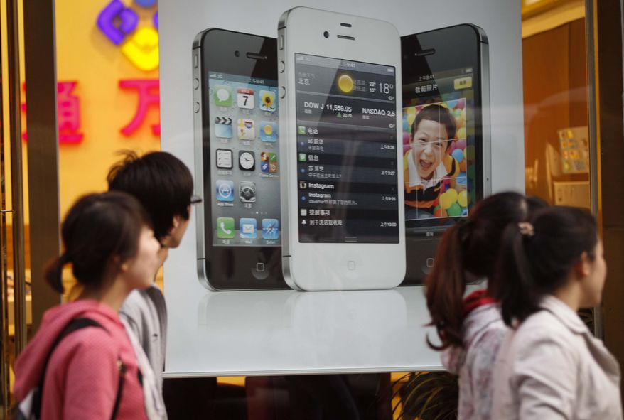 Chinese walk in front of an iPhone poster at a phone shop in Beijing Saturday, April 7, 2012. Authorities indicted five people in central China for involvement in illegal organ trading after a teenager sold one of his kidneys to buy an iPhone and an iPad. (AP Photo/ Vincent Thian)