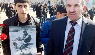 Aloysat Gasimov (right) was one of the first Azeri officials to reach the scene of the massacre in Khojaly 20 years ago. The student beside him holds a photo of Mr. Gasimov, now the head of a cultural center near the site of the 1992 massacre, kneeling next to a victim. (Eric J. Lyman/Special to The Washington Times)