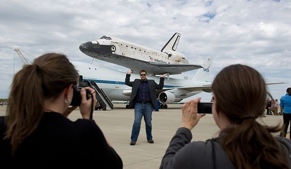 Joan Perry, of Stafor, Va., left, and Christine Rusbarsky, right, of Boston, Mass., photograph Brian Schuetz, center, as he pretends to lift the the space shuttle Discovery after it arrives by 747 carrier aircraft at Washington Dulles International Airport, Chantilly, Va., Tuesday, April 17, 2012. After completing 39 missions and spending 365 days in space, the historic spacecraft will make its final destination at the Steven F. Udvar-Hazy Center, a Smithsonian museum, located in Chantilly, Va., on Thursday, April 19. (Andrew Harnik/The Washington Times)
