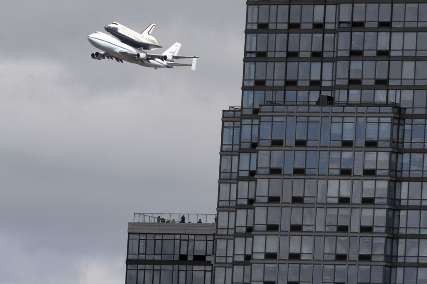 People watch from the balcony of a building as the space shuttle Enterprise, riding on the back of the NASA 747 Shuttle Carrier Aircraft, cruises over the Hudson river, Friday, April 27, 2012, in New York. Enterprise is eventually going to make its new home in New York City at the Intrepid Sea, Air and Space Museum. (AP Photo/Mary Altaffer)