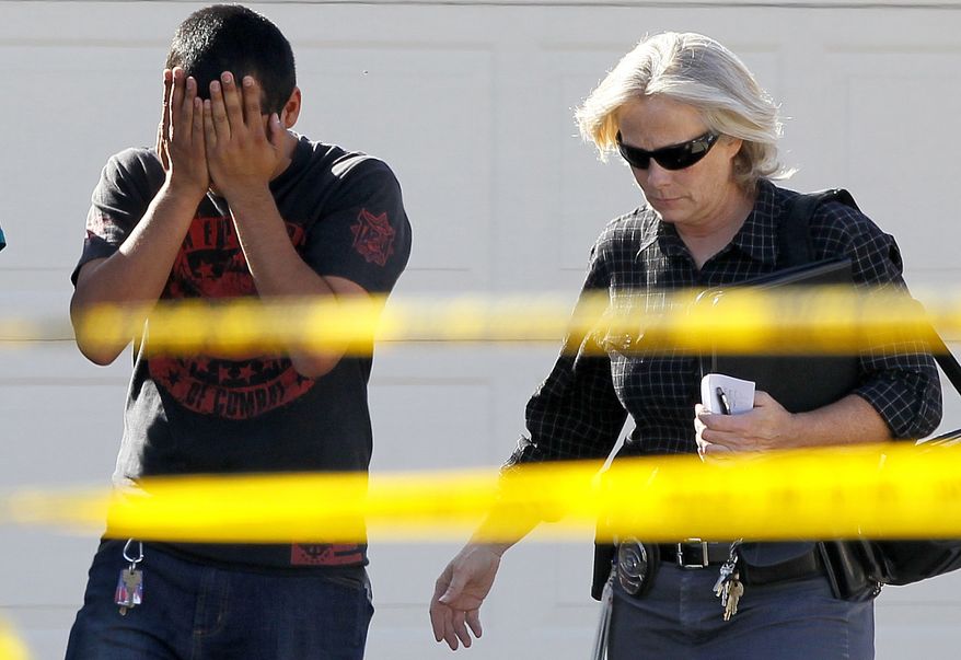 A police officer walks May 2, 2012, with a man who said he had a child inside of the home where five people were shot and killed in Gilbert, Ariz. Police identified one of the five people killed as a former Marine with ties to neo-Nazi and Minutemen groups. (Associated Press)