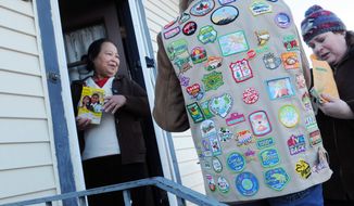 ** FILE ** A Girl Scout, wearing her vest covered in badges, sells a box of cookies to Paa Yang (left), a neighbor, in Minneapolis in 2012. (Associated Press)