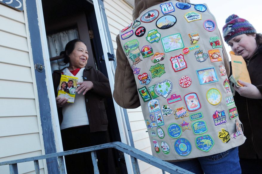 ** FILE ** A Girl Scout, wearing her vest covered in badges, sells a box of cookies to Paa Yang (left), a neighbor, in Minneapolis in 2012. (Associated Press)