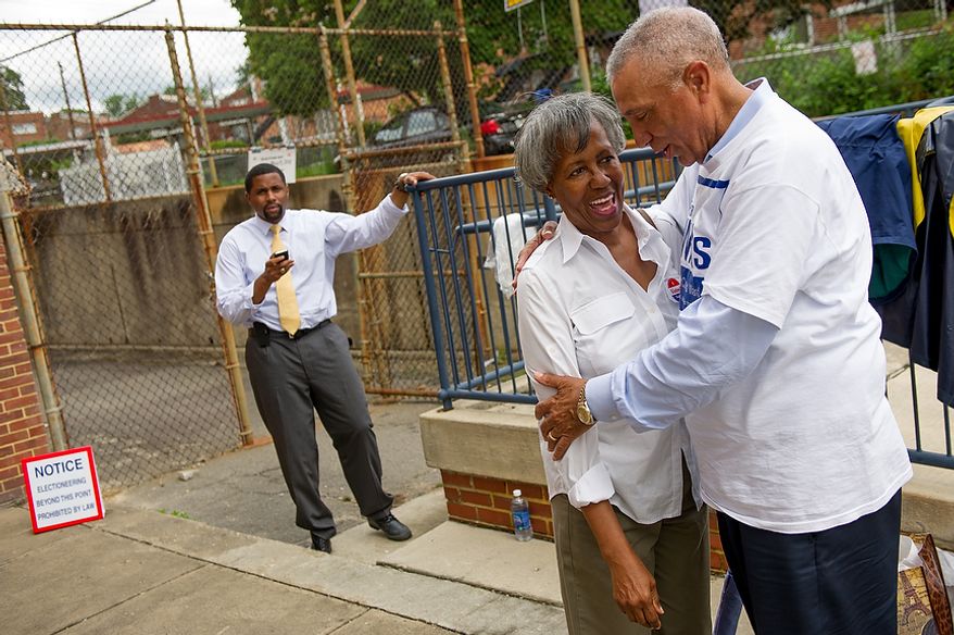 Candidate Delano Hunter, left, watches as candidate Frank Wilds, right, hugs D.C. resident Jean Johnson, outside a University of the District of Columbia Community College building, formerly Backus Middle School, on South Dakota Avenue in Northeast, Washington, D.C., Tuesday, May 15, 2012. Hunter and Wilds are two of the candidates running to replace Harry Thomas for Ward 5 city councilmember in a special election. (Andrew Harnik/The Washington Times)