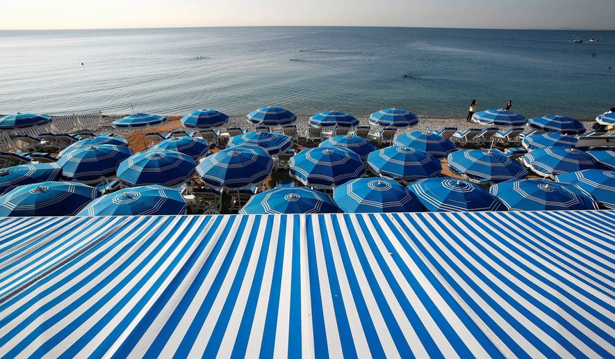 People swim in the Mediterranean Sea as blue beach umbrellas provide shade from the sun along the beach in Nice, southeastern France. (Associated Press) ** FILE **