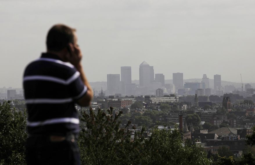 **FILE** A man talks on a mobile phone Sept. 23, 2011, as the high-rise buildings of the banks based in the Canary Wharf business district are seen in the distance from Parliament Hill on Hampstead Heath in London. (Associated Press)