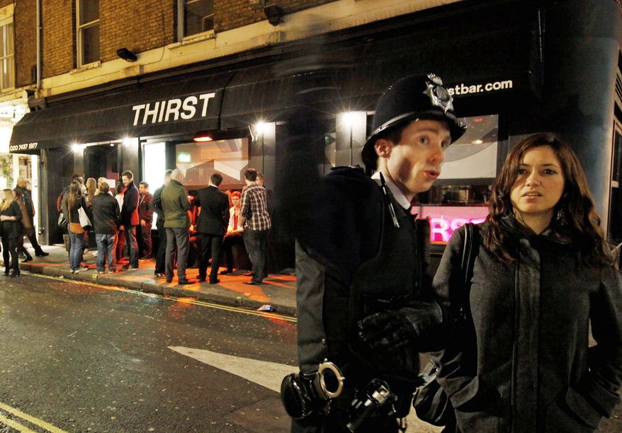 A man (top) is taken into the ambulance, known as a "booze bus," dedicated to keeping drunk people out of trouble on the streets and out of hospital emergency rooms, in the Soho area of central London. Binge drinking have caused a spike in health care costs and public displays of drunkenness. A policeman on patrol directs a young woman (above) in Soho. (Associated Press)