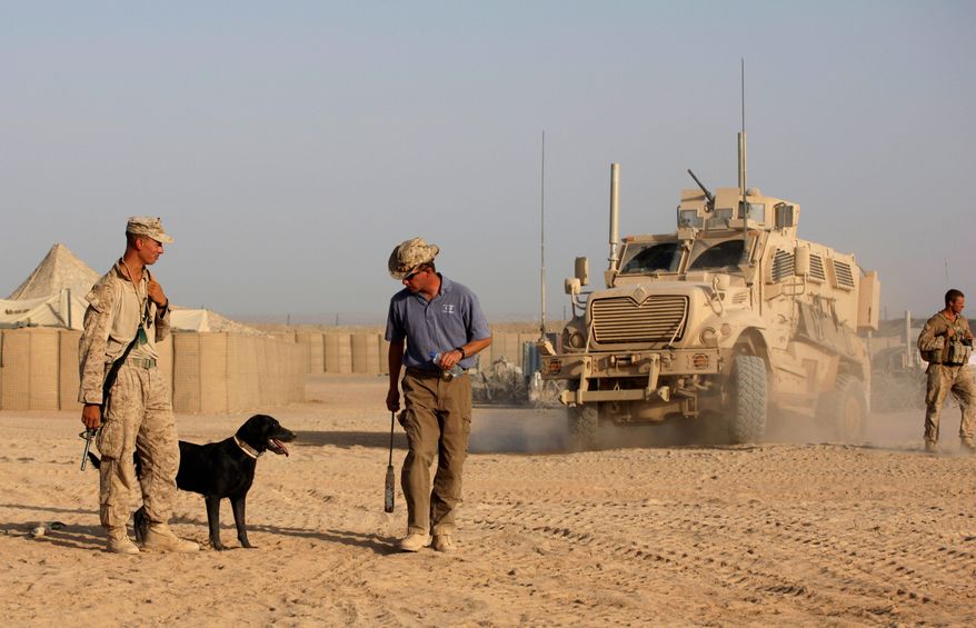 ** FILE ** Ringo, a bomb-sniffing dog, listens to trainer Adam Ward, a contractor working for American K-9 Interdiction, as dog handler Marine Cpl. William Childs observes in Helmand province, Afghanistan, in 2009. The Pentagon also has spent more than $200 million a year developing devices to detect roadside bombs. (Associated Press)