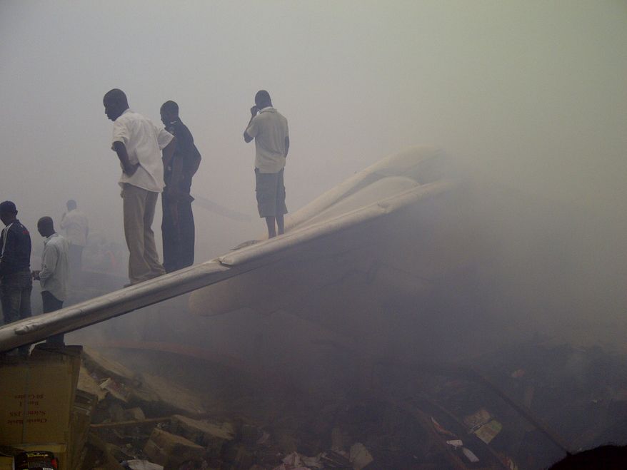 Onlookers stand on the tail wing of a crashed passenger plane in a neighborhood just north of Murtala Muhammed International Airport in Lagos, Nigeria, on Sunday, June 3, 2012. (AP Photo/Jon Gambrell)