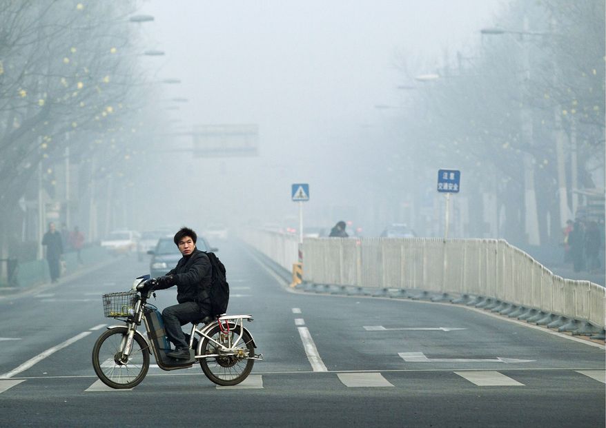 ** FILE ** In this June 5, 2012, file photo, a man rides an electric bike through the haze in Beijing. (Associated Press)