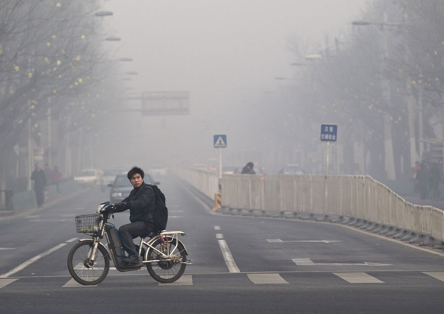 **FILE** A man rides an electric bike in Beijing Jan. 10, 2012, while crossing a street shrouded by haze. (Associated Press)