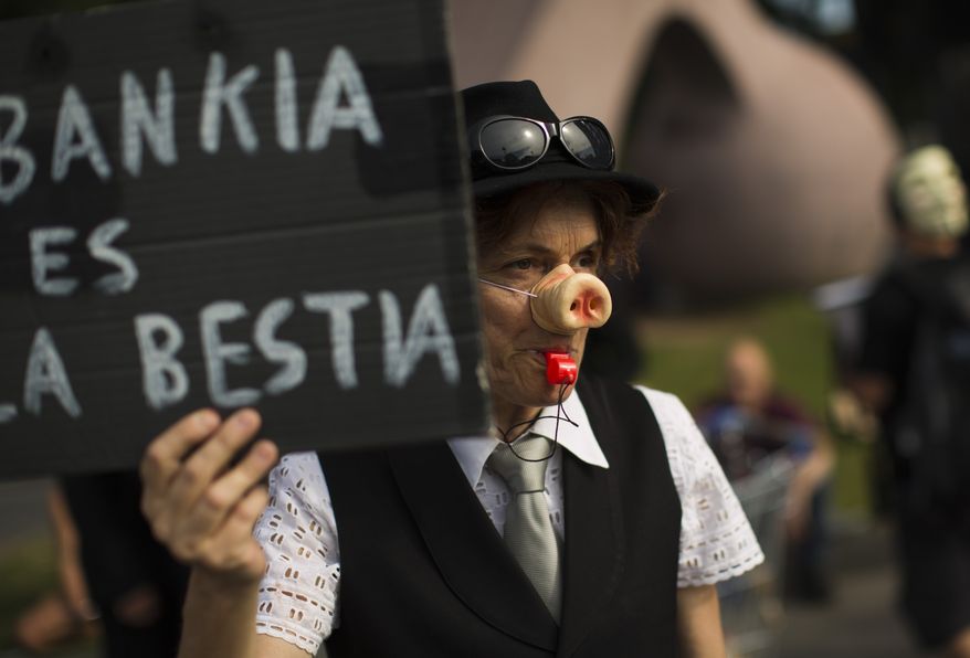 **FILE** A demonstrator holds a banner reading in Spanish "Bankia is a wild animal" during a demonstration June 2, 2012, next to a Bankia bank branch in Barcelona. (Associated Press)