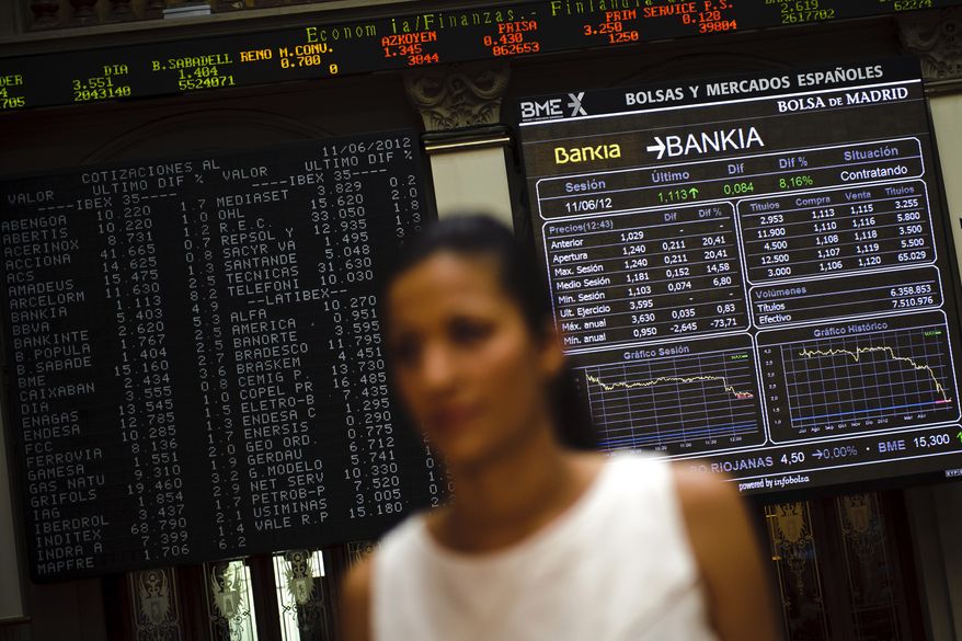 A journalist stands live June 11, 2012, on TV in front of the Stock Exchange's main display in Madrid as it shows Bankia values. (Associated Press)