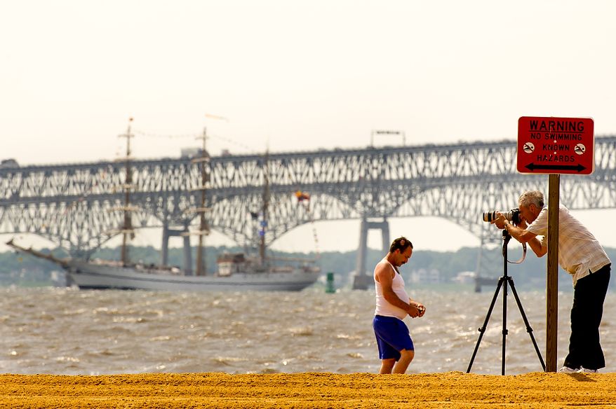 Joe Hennessy (right) of Adelphi, Md., takes photographs June 13, 2012, from the beach at Sandy Point State Park in Annapolis, Md., of tall ships passing under the Chesapeake Bay Bridge en route to the Inner Harbor in Baltimore for a bicentennial commemoration of the War of 1812. The week-long "Star-Spangled Sailabration" includes free tours of the ships, waterside festivities, an air show featuring the Blue Angels and the world premiere of "Overture for 2012," composed by Philip Glass. (Andrew Harnik/The Washington Times)