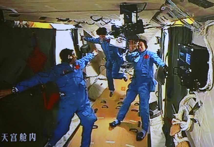 In this image made June 18, 2012, off the monitor screen at the Beijing Aerospace Flight Control Center and released by China's Xinhua News Agency, Chinese astronaut Liu Wang (left) tries to help his female colleague Liu Yang move forward as their commander Jing Haipeng waves in the orbiting Tiangong-1 lab module. They moved from Shenzhou-9 spacecraft to this module three hours after docking earlier that day. (Associated Press/Beijing Aerospace Control Center via Xinhua)