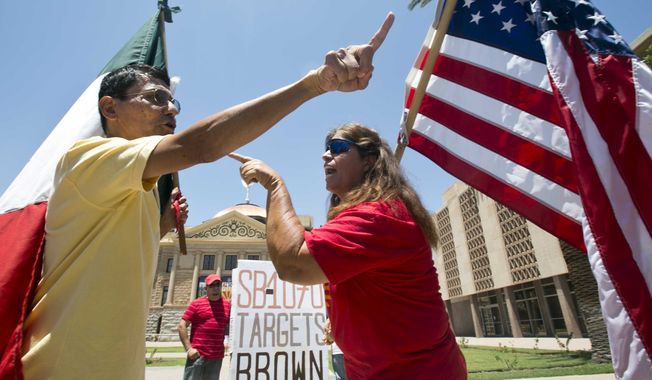 Andy Hernandez, carrying a Mexican flag (left), and Allison Culver, carrying an American flag, argue over Arizona&#x27;s immigration law outside the State Capitol Building in Phoenix, Ariz. While finding much of the Arizona law unconstitutional, the U.S. Supreme Court said Monday that one part would stand — the portion requiring police to check the status of someone they suspect is not in the United States legally. (Arizona Republic via Associated Press)