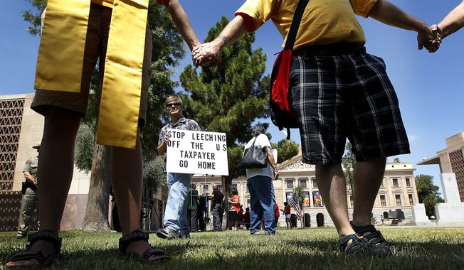 An immigration rights opponent walks around June 25, 2012, with a sign at the Arizona Capitol in Phoenix as people react to the Supreme Court decision regarding Arizona&#x27;s controversial immigration law. The court struck down key provisions of the state’s crackdown on immigrants, but said a much-debated portion on checking suspects&#x27; status could go forward. (Associated Press)