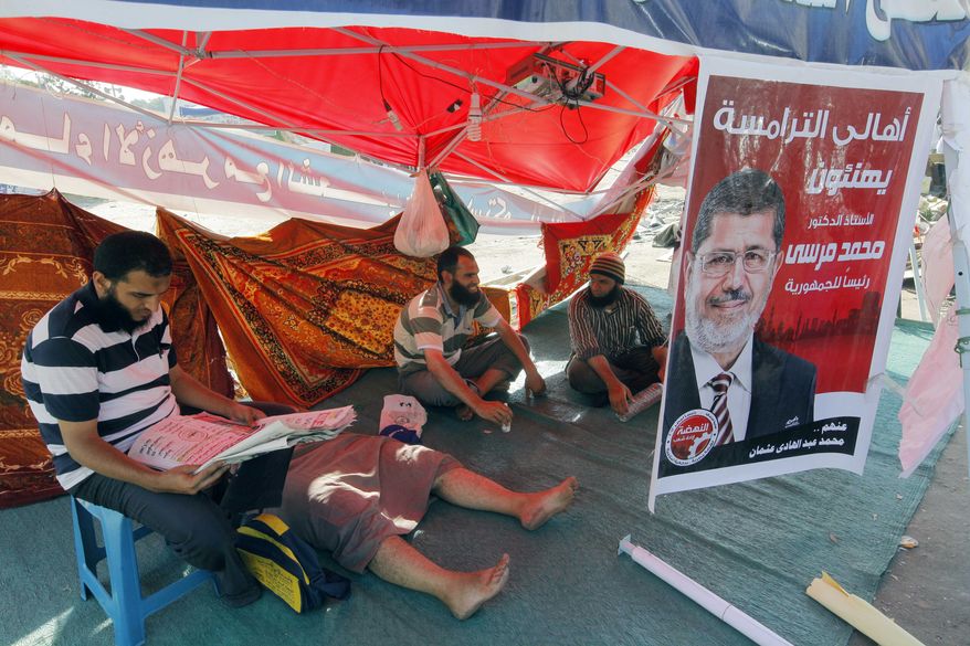 Egyptian protesters sit June 28, 2012, in Cairo's Tahrir Square at a camp fronted by a poster of Egypt's president-elect Mohammed Morsi, who was declared Egypt's first freely elected president in modern history four days earlier. The Arabic on the poster reads, "Mohammed Morsi for Egyptian presidency." (Associated Press)