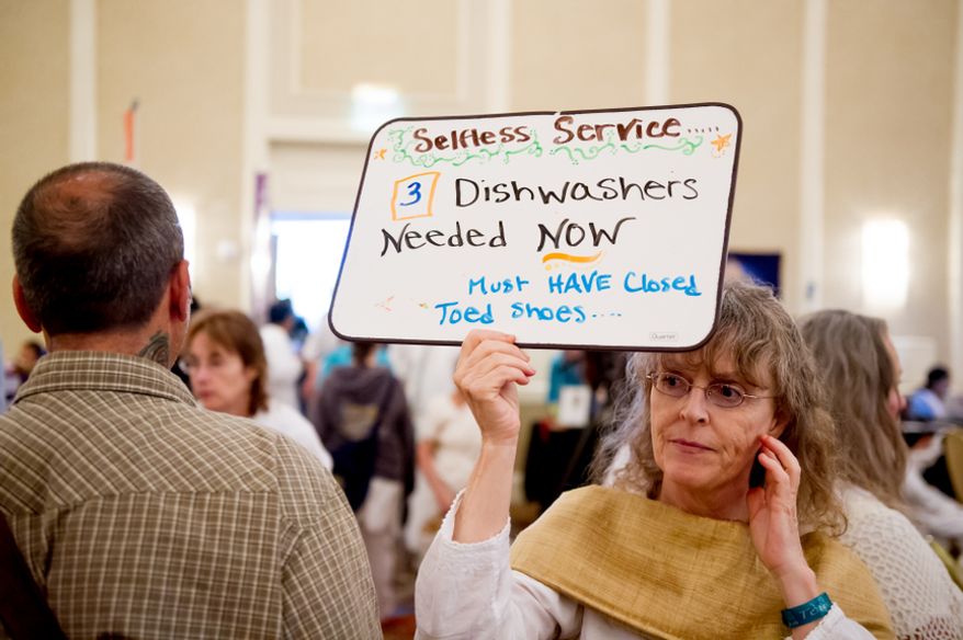 Volunteer Kerry Fitzpatrick of Seattle, Wash. walks around with a sign asking for help washing dishes as spiritual leader Mata Amritanandamayi, also known as "Amma" or the "Hugging Saint," hugs and blesses followers at the Hilton Alexandria Mark Center, Alexandria, Va., Friday, July 6, 2012. (Andrew Harnik/The Washington Times)