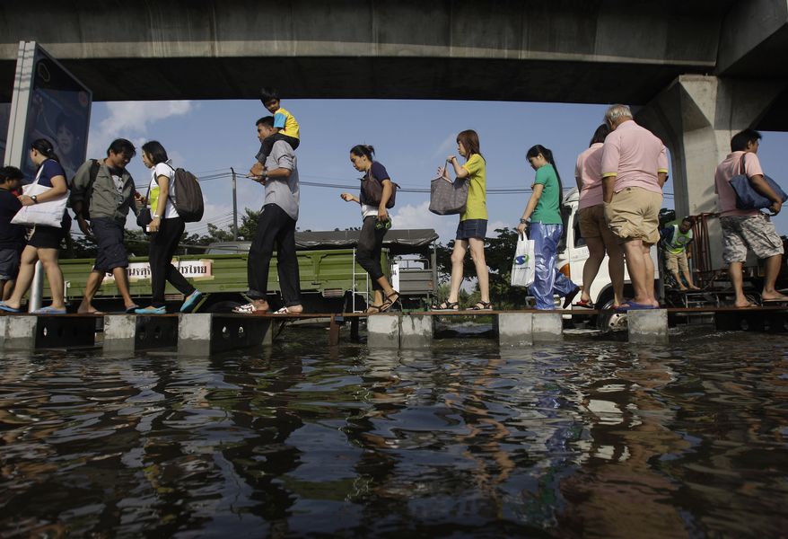 **FILE** Pedestrians use an elevated makeshift walkway to avoid the floodwaters in Bangkok on Nov. 10, 2011. (Associated Press)