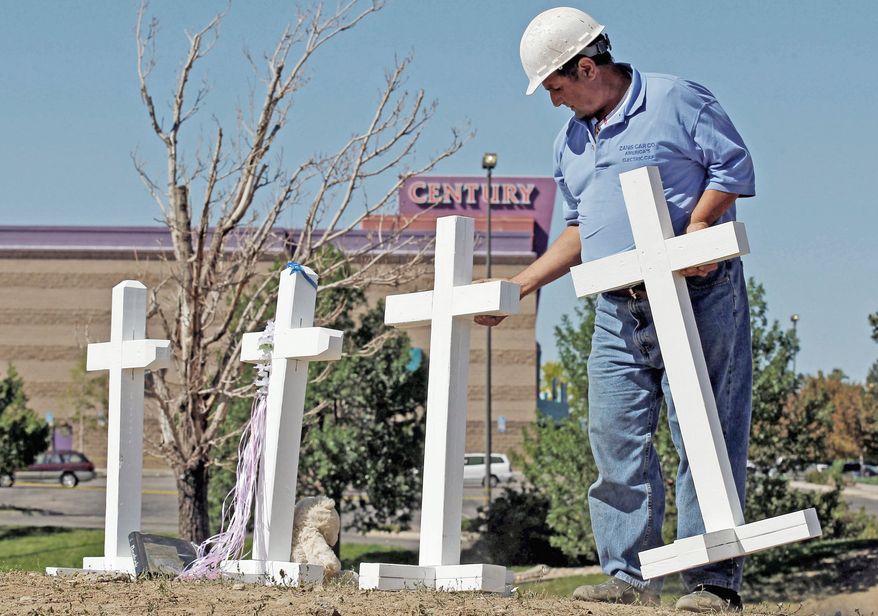 ** FILE ** Greg Zanis of Aurora, Ill., places 12 crosses, one for each shooting victim, across the street from the Century 16 movie theater in Aurora, Colo., on Sunday, July 22, 2012. (Associated Press)