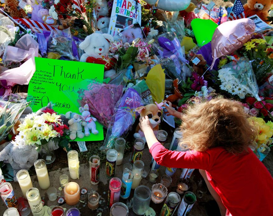 Serenity Brydon, 7, on Sunday places a rosary at a memorial near the Century 16 movie theater in Aurora, Colo. Twelve people were killed and 58 were injured in a shooting attack early Friday. (Associated Press)