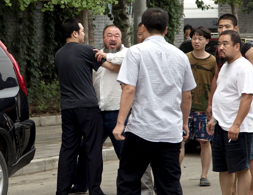 Ai Weiwei, second from left, stopped by a plain clothes policeman while he argues with another policeman, foreground, outside his home in Beijing Wednesday, June 20, 2012. Chinese police on Wednesday barred Ai from attending the first hearing of a lawsuit brought by his company against Beijing tax authorities and blocked reporters from filming at the courthouse, part of an intimidation campaign aimed at silencing the prominent artist and outspoken government critic. (AP Photo/Andy Wong)