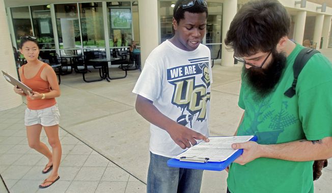 Aubrey Marks (left) looks on Tuesday at the University of Central Florida in Orlando, Fla., as Jordan Allen (center) helps student Casey Eirhstaedt register to vote. While most college campuses are relatively quiet, students at UCF have taken it upon themselves to register peers during the summer. (Associated Press)