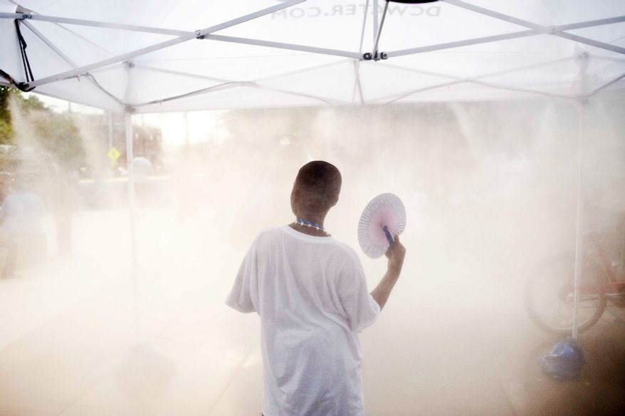 Attendees stay cool by waking through a mist tent during the Seven District's National Night Out. The annual event features community awards, crime prevention initiatives, health and wellness screenings and safety demonstrations and games. (Raymond Thompson/The Washington Times)