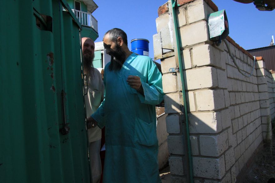 Members of an underground sect in Russia's Volga River province of Tatarstan province stand at the gate of a house outside the provincial capital, Kazan, on Aug. 8, 2012. The reclusive sect that literally went underground to stop contact with the outside world kept 27 children in dark and unheated cells, many of them for more than a decade, prosecutors said. (Associated Press)