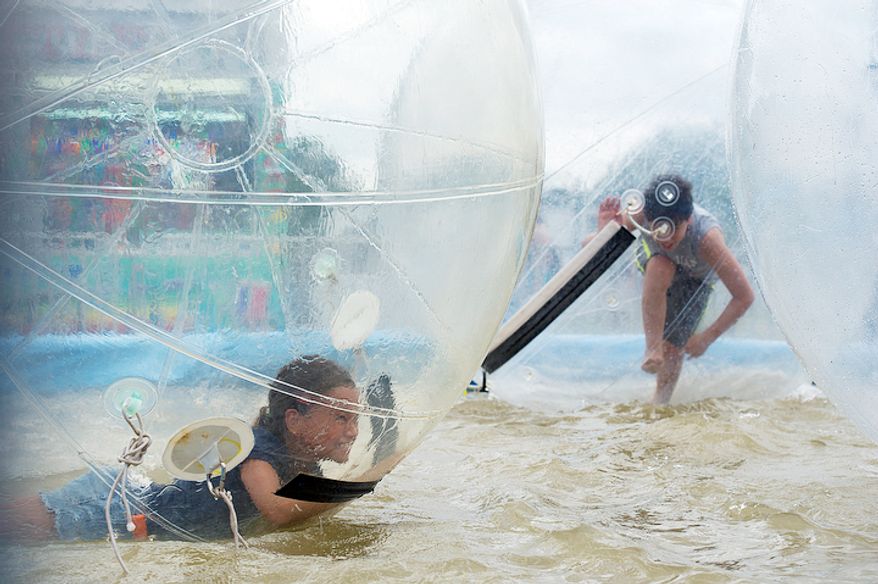 Isabelle Brown, left, 9, of Arlington laughs as she tries to get back up in the "Euro Bobbles" at the Arlington County Fair. The bobbles resembled giant hamster balls that were filled with air. (Barbara L. Salisbury/The Washington Times)
