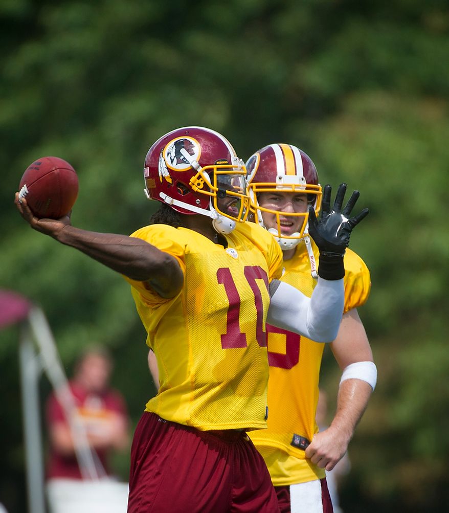 With Rex Grossman (right) looking on Robert Griffin III makes a pass during the Redskins training camp at Redskins Park in Ashburn, Va., Monday, August 13, 2012. (Rod Lamkey Jr./The Washington Times)