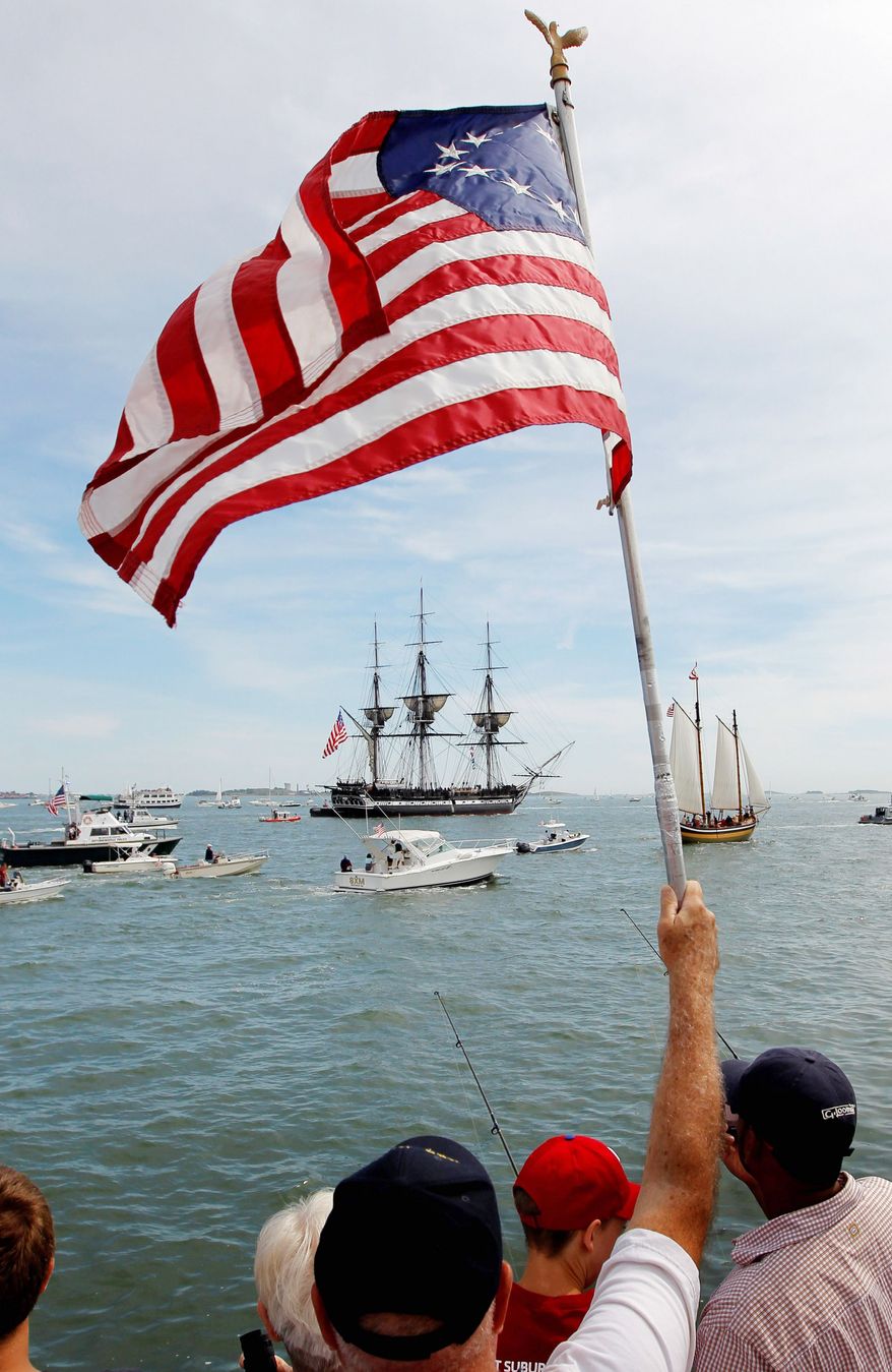 An onlooker waves a Colonial-era flag as the USS Constitution passes through Boston Harbor on Sunday. The USS Constitution’s sailing commemorated the 200th anniversary of the ship’s victory over the HMS Guerriere in the War of 1812. (Associated Press)
