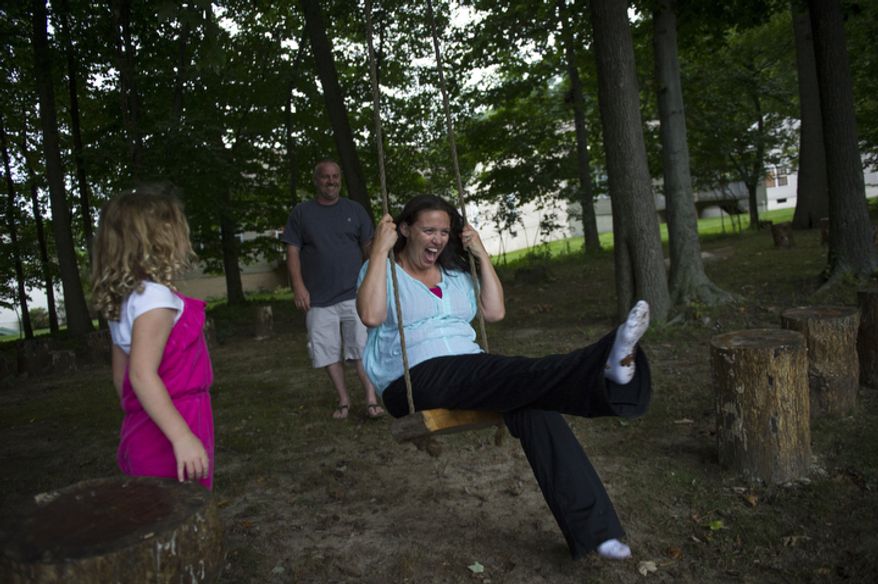 With their daughter Catalina, 5, looking on, Joe Carr pushes his wife Sofia on a swing in their backyard after sitting for a portrait at their home in Downingtown, Pa. (Rod Lamkey Jr./The Washington Times)