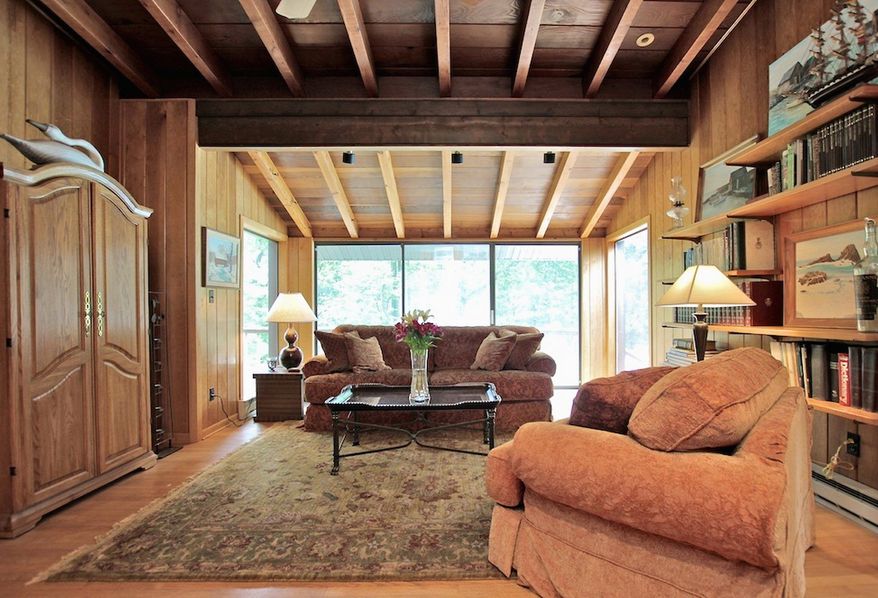 The living room has a wall of glass doors and a wood-beamed cathedral ceiling. It also features a stone fireplace.