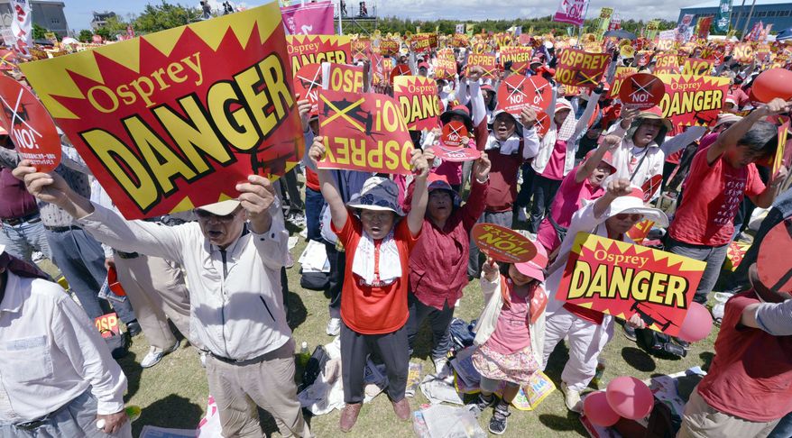 Japanese protesters raise signs Sunday at a seaside park on Okinawa to oppose U.S. plans to deploy 12 MV-22 Osprey aircraft on the island. Safety concerns boiled over after Osprey crashes in Morocco and Florida earlier this year. (Associated Press)
