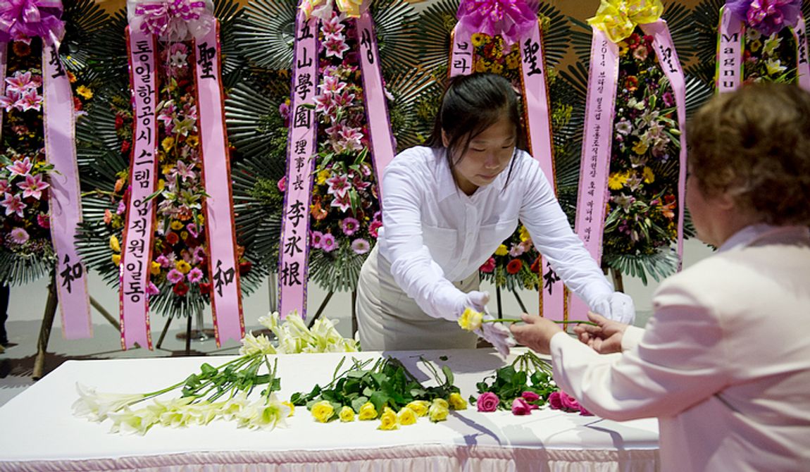 A volunteer hands a rose to a mourner at the Cheongpyeong Heaven and Earth Training Center complex on Wednesday, Sept. 12, 2012 so that the mourner can place it as an offering on a table beneath a portrait of the late Rev. Sun Myung Moon. Thousands of mourners have come to the complex near Seoul, Korea to pay their respects to the reverend, who founded the Unification Church. (Barbara L. Salisbury/The Washington Times)