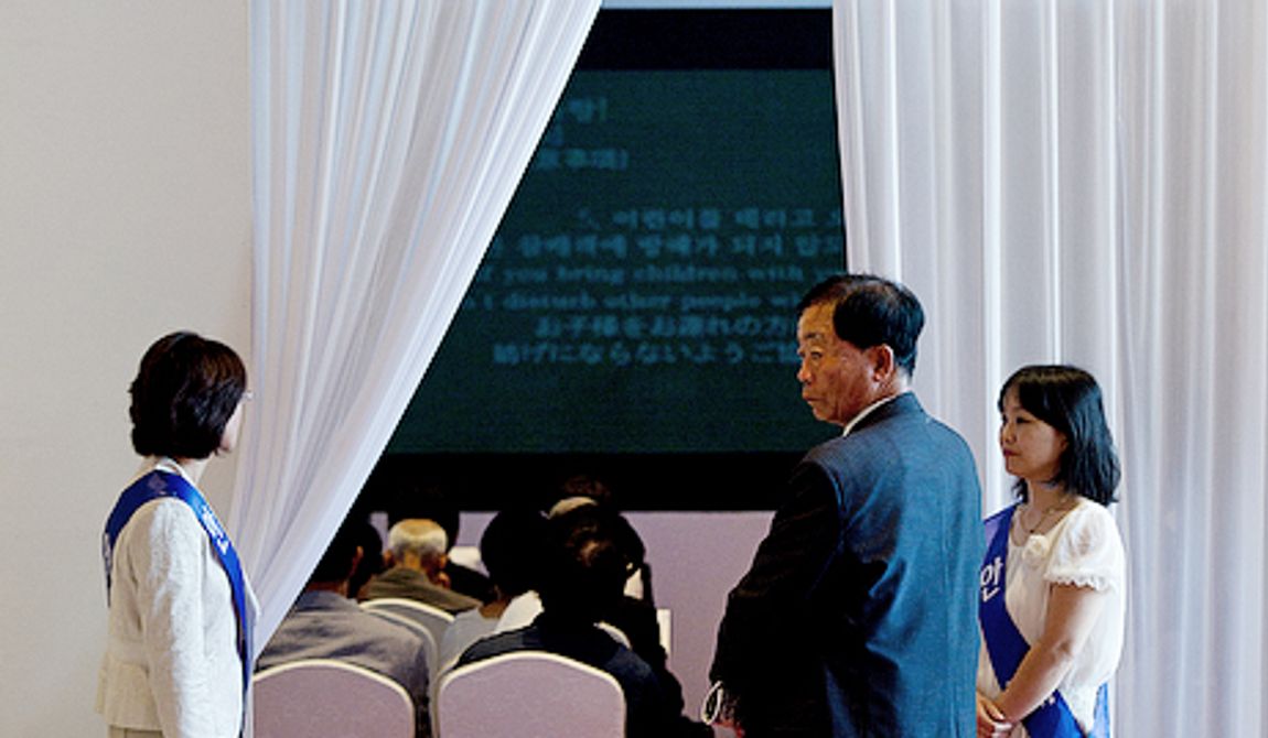 Ushers hold open a curtain that leads into a room to watch a video presentation on the life of the Rev. Sun Myung Moon inside the Cheongpyeong Heaven and Earth Training Center complex near Seoul, Korea on Wednesday, Sept. 12, 2012. Thousands of mourners have come over the past few days to pay tribute to the reverend. Once inside the complex, they first watched the video on his life, then signed in electronically before being given flowers to offer and the chance to write a remembrance on a special wall. (Barbara L. Salisbury/The Washington Times)