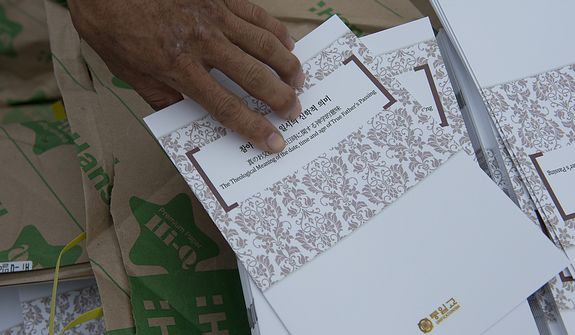 A mourner picks up a program for the Seonghwa, or ascension, ceremony, known as the traditional funeral in western terms, for the late Rev. Sun Myung Moon Saturday, Sept. 15, 2012 at the Cheong Shim Peace World Center in Gapyeong, Korea. Thousands of mourners from countries around the world came to witness the event and say goodbye to the head of the Unification Church. Some 15,000 fit into the stadium, where the funeral was held, with another 10,000 to 15,000 expected to be watching live simulcasts around the complex. (Barbara L. Salisbury/The Washington Times)
