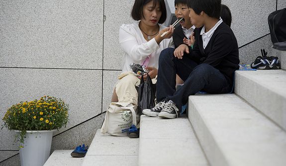 A mother feeds her children on the steps of the stadium outside the Cheong Shim Peace World Center in Gapyeong, Korea on Saturday, Sept. 15, 2012. Because thousands of mourners from countries around the world came to witness the event and say goodbye to the head of the Unification Church, the late Rev. Sun Myung Moon, many arrived very early and took a break to eat once there. (Barbara L. Salisbury/The Washington Times)