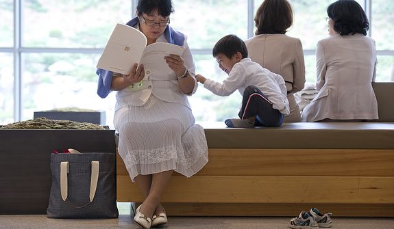 A little boy tries to get this older woman&#39;s attention as she is reading the program for the funeral for the late Rev. Sun Myung Moon inside the stadium of the Cheong Shim Peace World Center in Gapyeong, Korea on Saturday, Sept. 15, 2012. (Barbara L. Salisbury/The Washington Times)