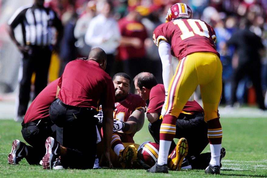 Washington Redskins tackle Trent Williams (71) sits injured on the field as quarterback Robert Griffin III (10) looks on at FedEx Field. (Preston Keres/Special to The Washington Times)