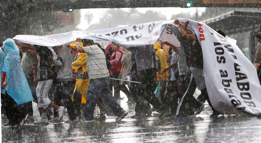 Protesters shield themselves from the rain with a banner as they demonstrate Thursday against proposed labor reforms in Mexico City. Supporters say, however, that the bill would support creation of the million jobs a year the country needs for its young people and migrants returning from the U.S. (Associated Press)