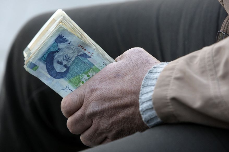 **FILE** An Iranian street money changer holds Iranian banknotes with a portrait of late revolutionary founder Ayatollah Khomeini in the main old Bazaar of Tehran. (Associated Press)