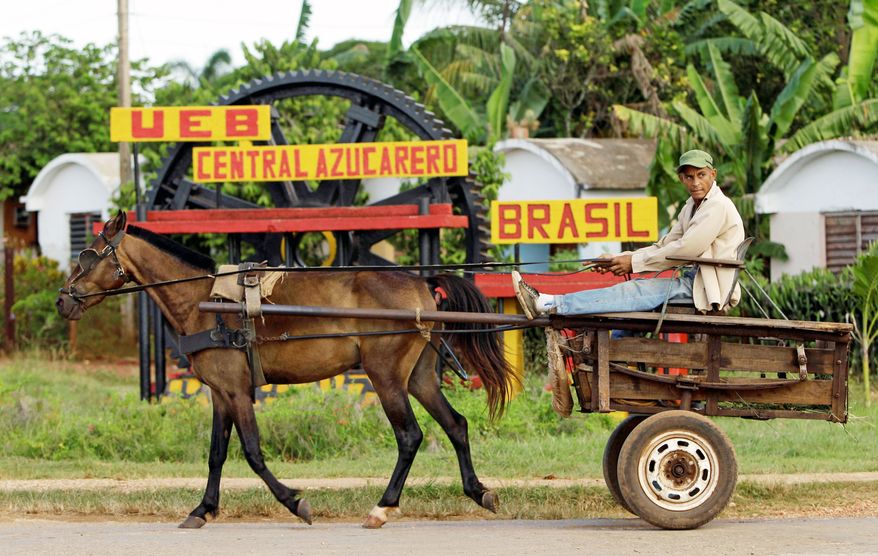 A rider in a horse-drawn carriage passes outside the Brasil sugar processing plant in Jaronu, Cuba, where a worker walks among old machinery. (Associated Press)