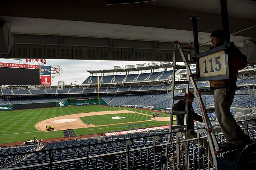 Stadium workers Peter Gabauer (right) and Wes Snyder (bottom left) take down a sign to make way for an extra camera platform along the third base stands as crews get ready for game 3 at Nationals Park as the Washington Nationals take on the St. Louis Cardinals in the first round of the Major League Baseball playoffs in Washington on Monday, Oct. 8, 2012. (Andrew Harnik/The Washington Times)