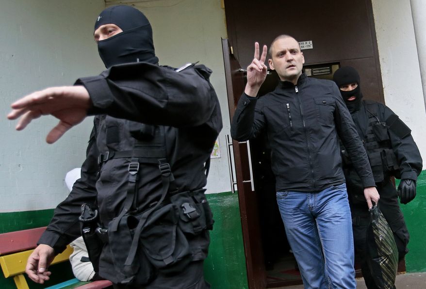 Russian opposition leader Sergei Udaltsov (center) gestures as masked police officers take him for questioning in Moscow on Wednesday, Oct. 17, 2012. In a new sign of a widening crackdown on Russia's opposition, investigators have opened a criminal probe against Mr. Udaltsov and several other activists for allegedly plotting mass riots. (AP Photo/Mikhail Metzel)