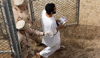 Guards escort a Guantanamo detainee carrying a book at the Camp 4 detention facility&#x27;s open-air common area at the U.S. naval base in Guantanamo Bay, Cuba, on Nov. 18, 2008. (AP Photo/Brennan Linsley) ** FILE **