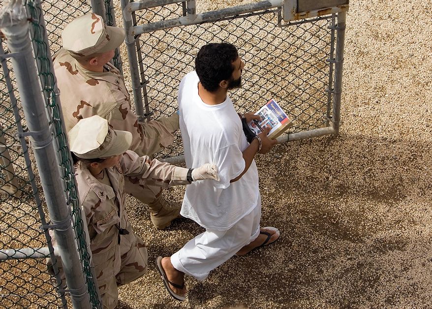 Guards escort a Guantanamo detainee carrying a book at the Camp 4 detention facility&#x27;s open-air common area at the U.S. naval base in Guantanamo Bay, Cuba, on Nov. 18, 2008. (AP Photo/Brennan Linsley) ** FILE **